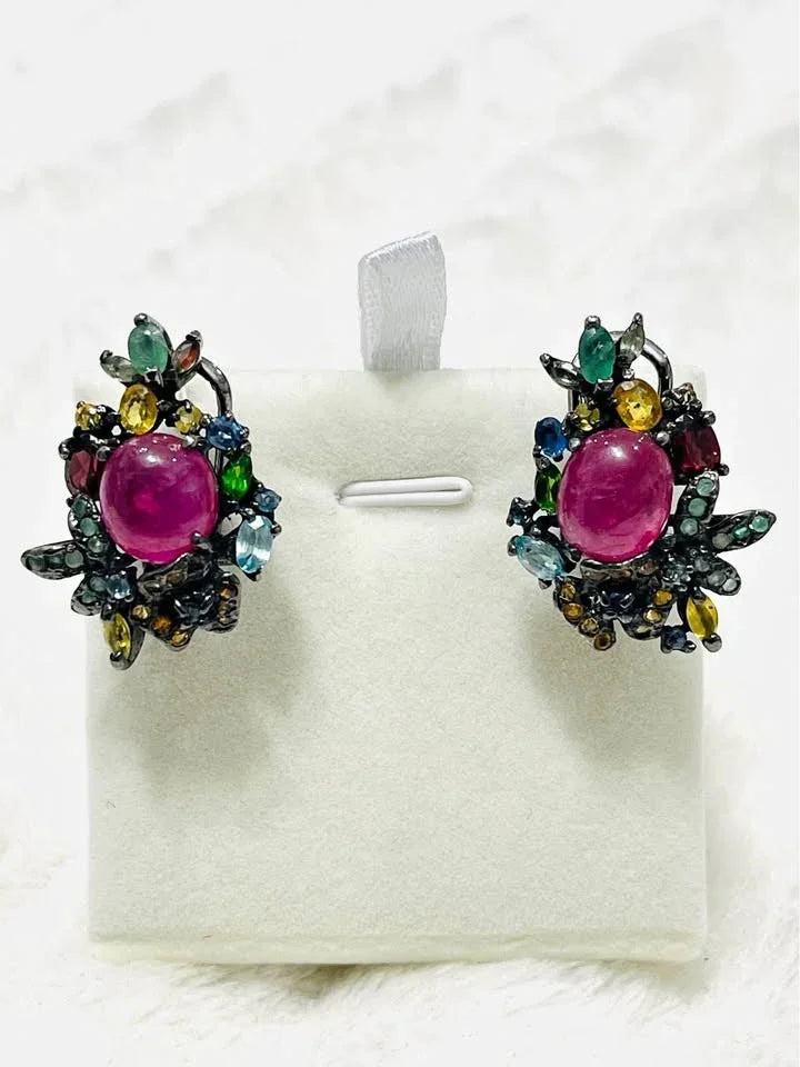 A pair of post-style earrings with natural rubies, emeralds, and sapphires, artfully arranged in a floral design.