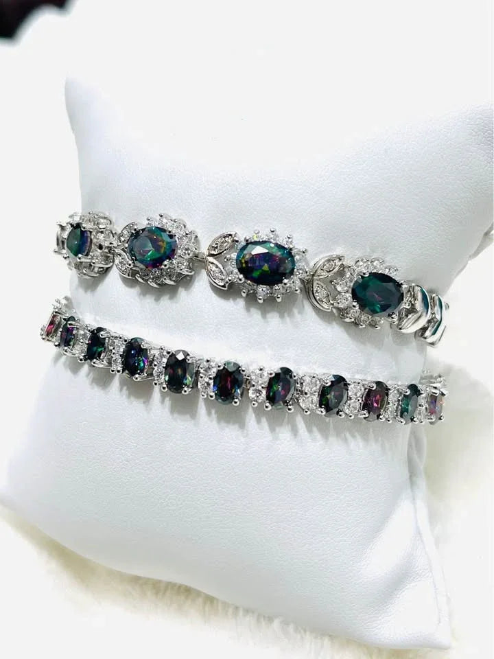 Side view of two striking mystic topaz sterling silver bracelets, one a tennis style, on a white jewelry display.