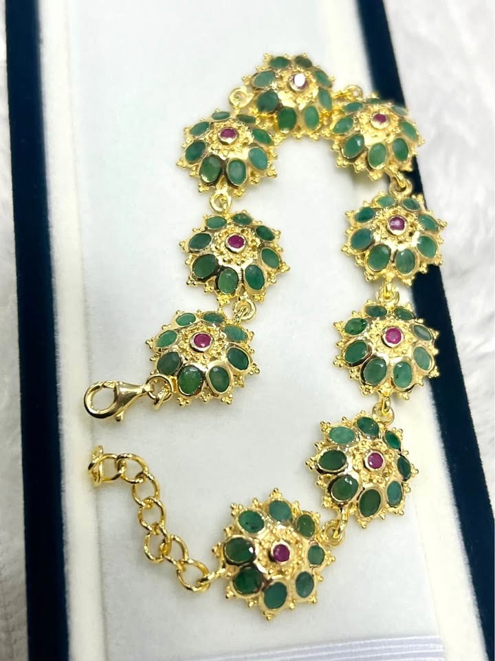 Gold floral bracelet with natural emeralds and rubies. Angled view highlighting the intricate links and clasp.