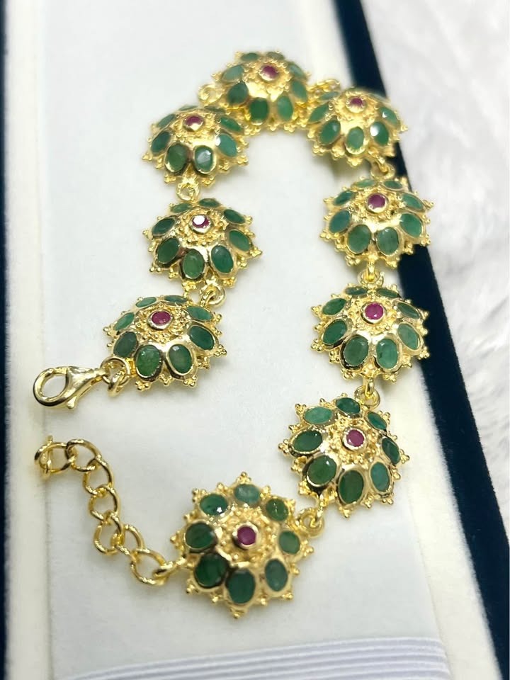 Angled view of a beautiful gold bracelet featuring natural Colombian emeralds and ruby centers.