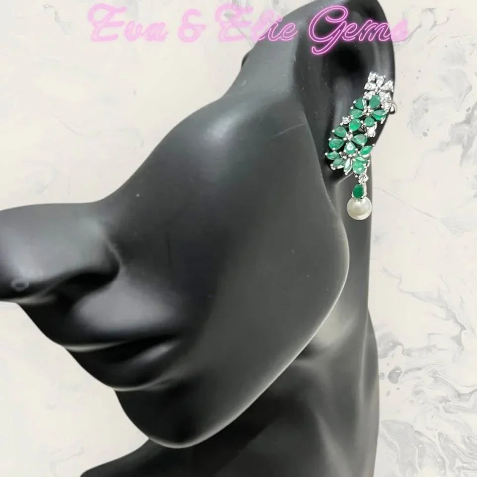 Natural emerald ear climber with pearl on mannequin, showcasing design against a marble-like background.