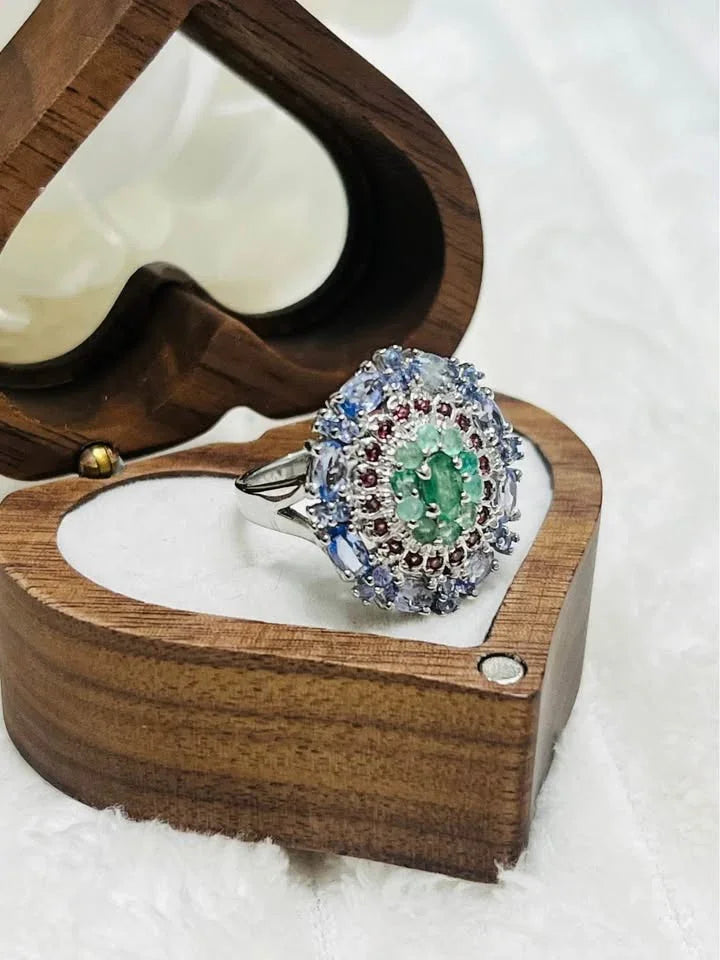  A side-angle view of a natural emerald, rhodolite, and tanzanite ring in a heart-shaped wooden box.