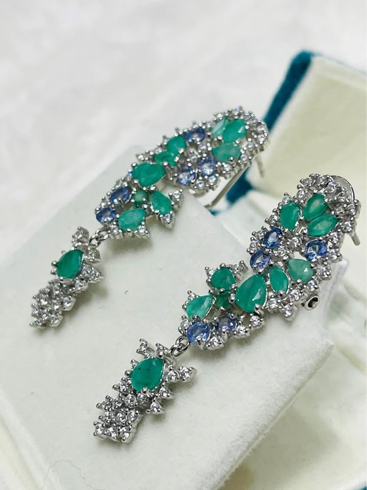A pair of fancy earrings with natural emeralds, tanzanites, and clear stones, showcasing a complex floral design.