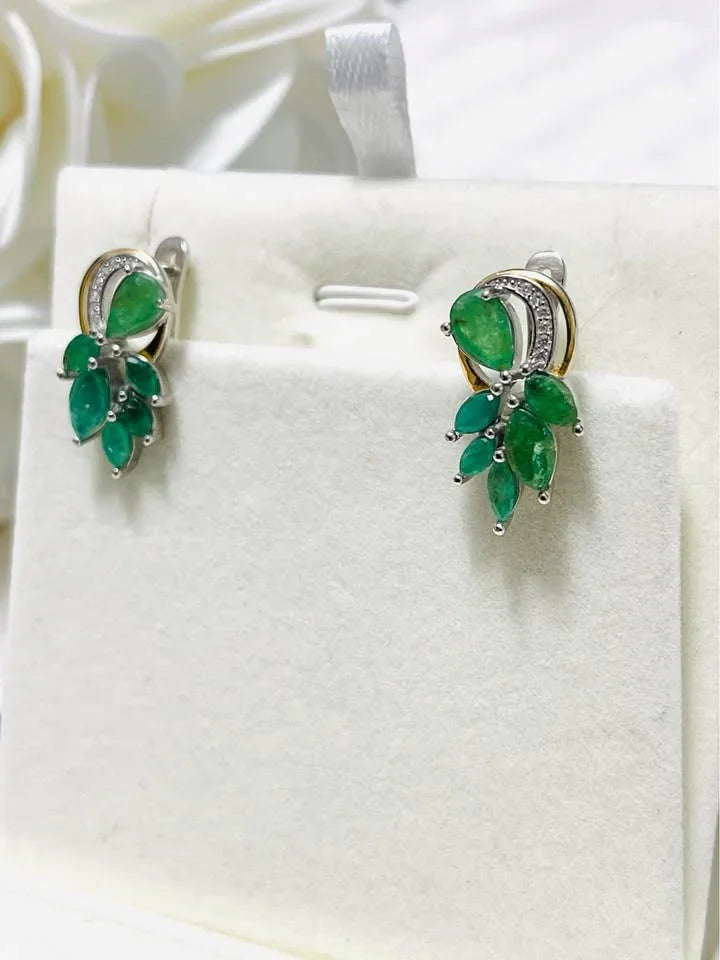 An angled view of natural sterling silver and gold earrings with a cluster of vibrant emeralds.