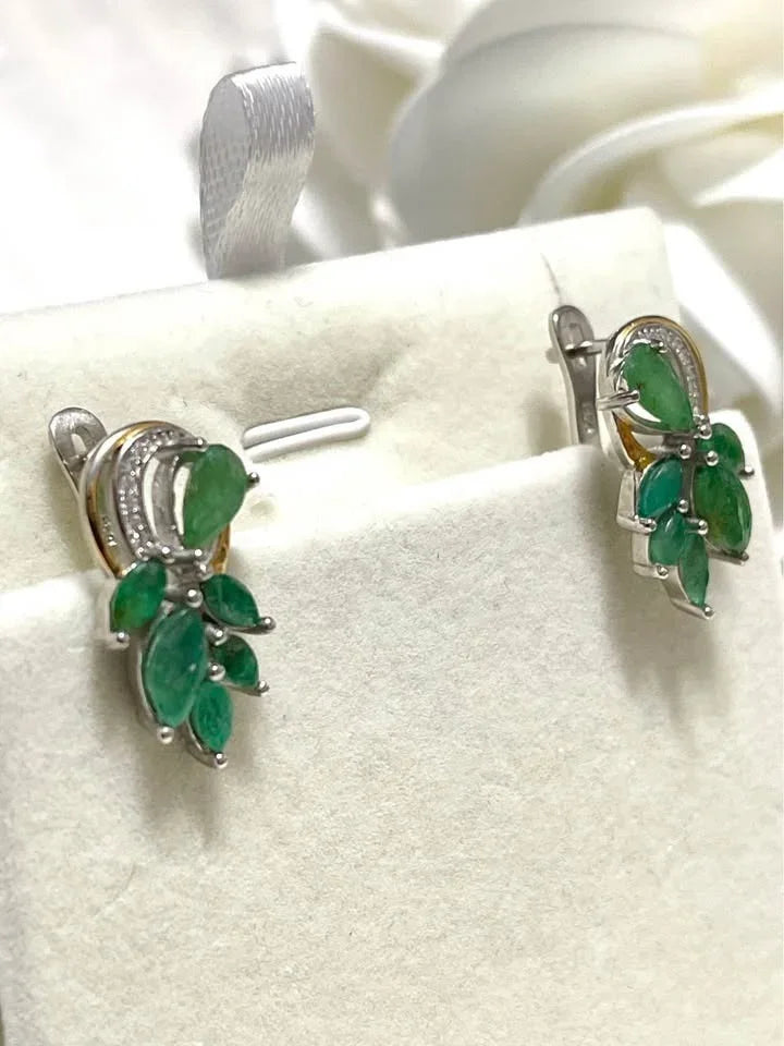 A close-up of natural sterling silver emerald earrings, showing the two-toned gold and silver detail.