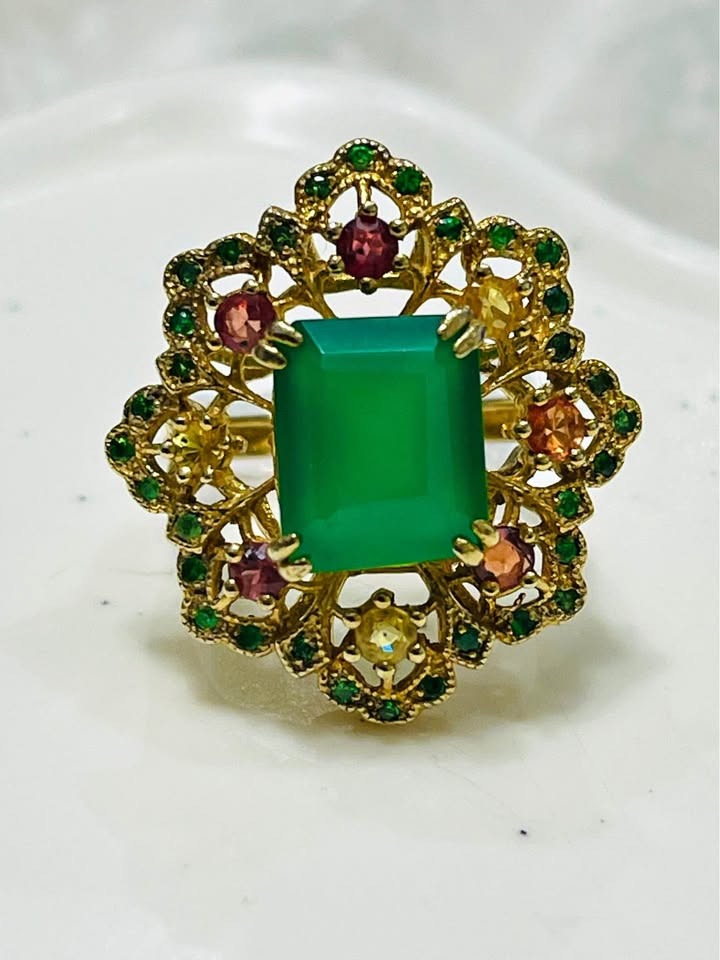 A stunning gold ring with a vibrant natural green agate, complemented by small emeralds, sapphires, and diopside stones.