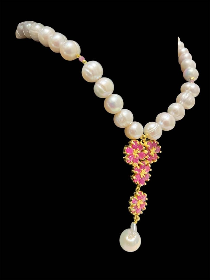 Beautiful natural freshwater pearl necklace with a ruby floral lariat-style drop on dark background.
