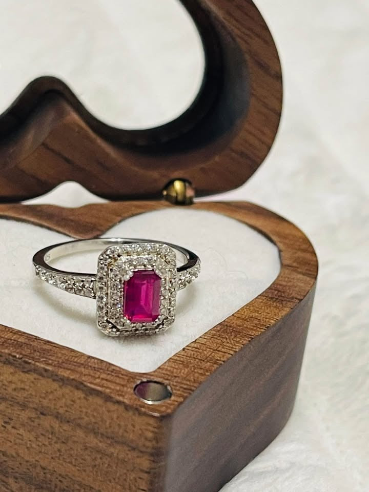 Natural ruby and diamond halo ring with a radiant emerald cut ruby, displayed in a wooden heart-shaped box.