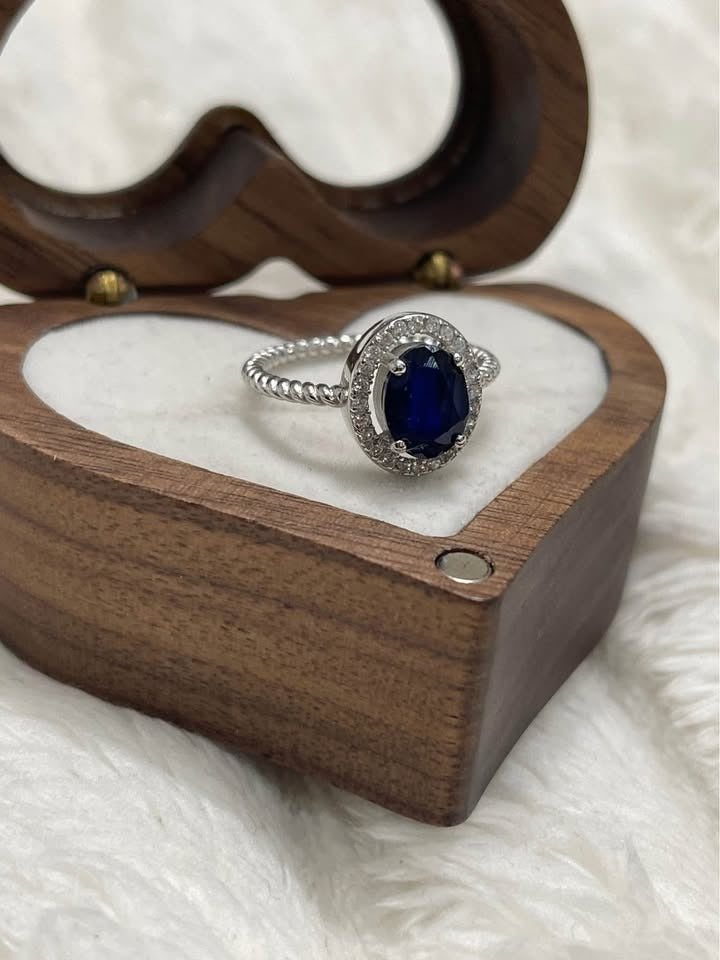 Natural 2ct sapphire solitaire ring with diamond halo and twisted band, sitting in a heart-shaped wooden box.