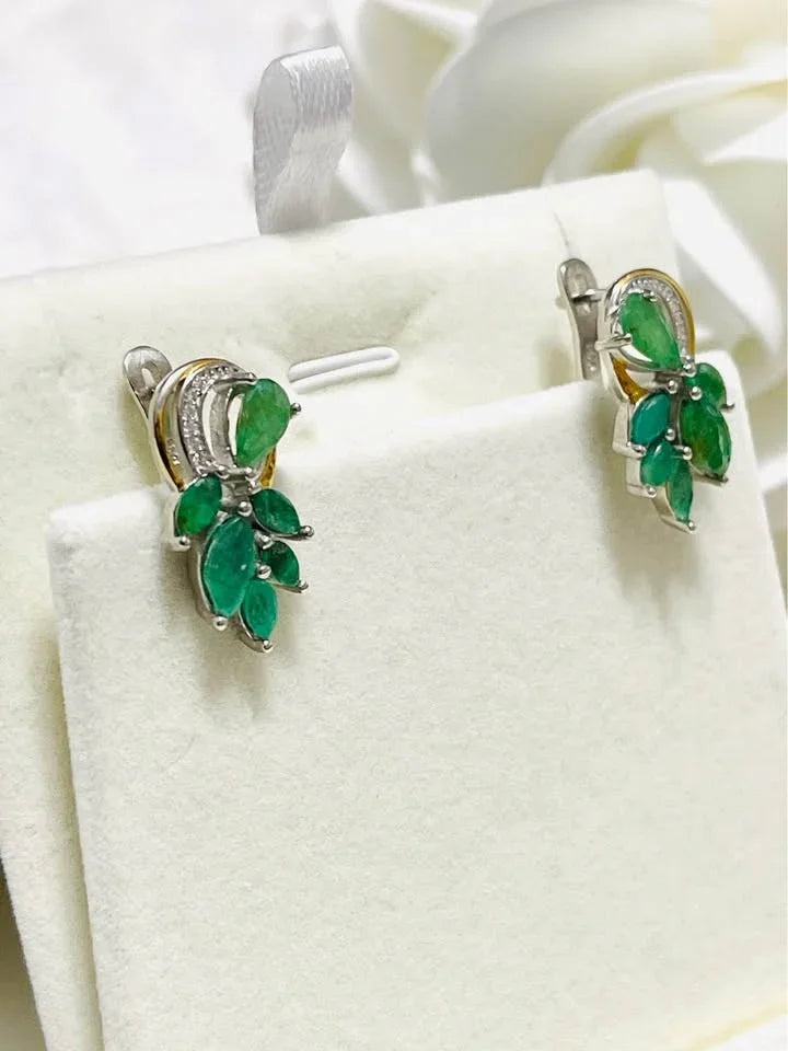 Natural sterling silver earrings with green emeralds and subtle two-toned gold accents on a white background.