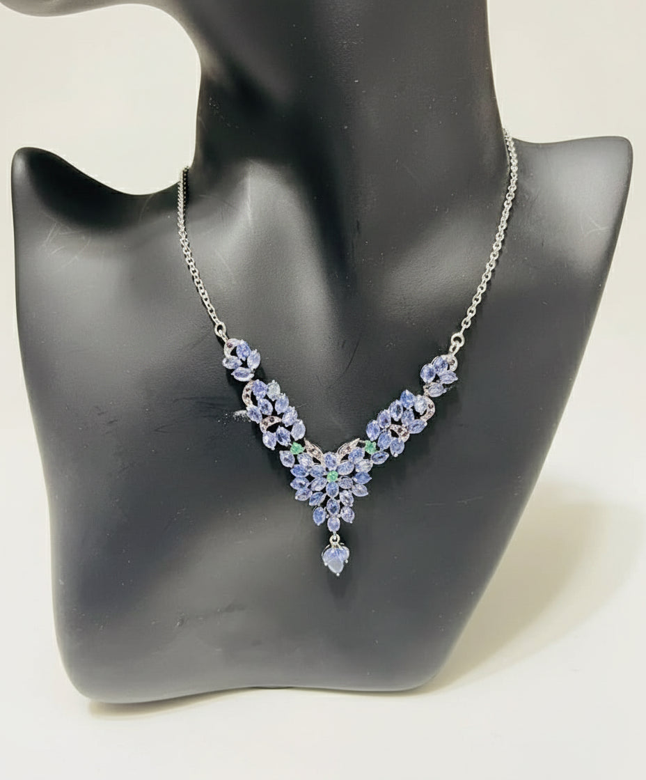 A natural tanzanite and emerald necklace with a floral design, crafted in sterling silver and displayed on a mannequin.