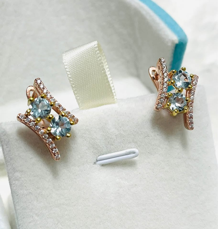 Close-up of natural blue topaz earrings with rose gold and diamond accents, sitting in a jewelry box.