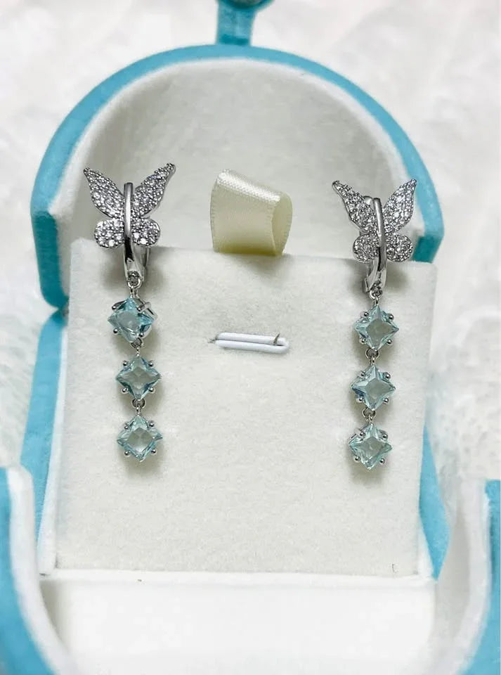 A pair of new butterfly dangle earrings with sparkling stones and three square-cut blue gemstones.