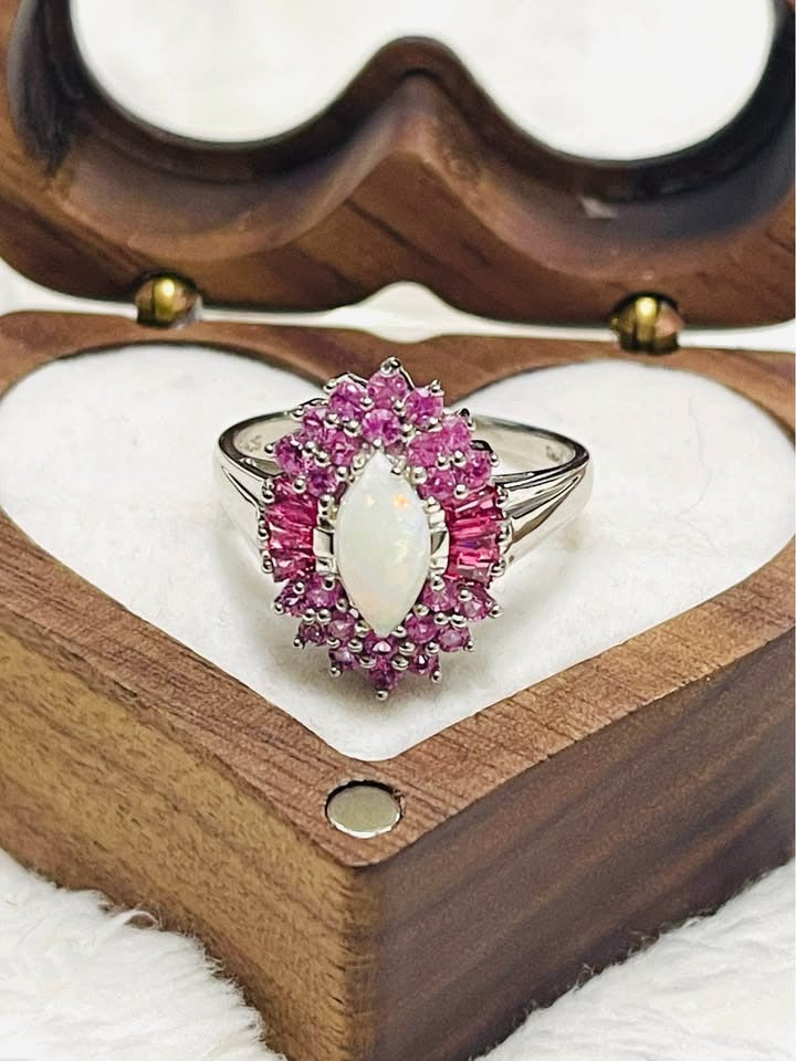 An exquisite Australian opal ring with a pink sapphire halo, displayed in a heart-shaped wooden jewelry box.