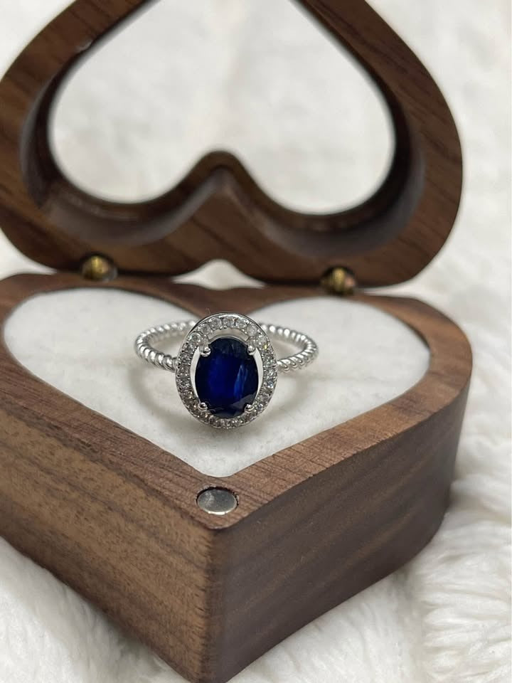 Stunning 2 carat oval blue sapphire ring with a diamond halo, displayed in a decorative wooden heart box.