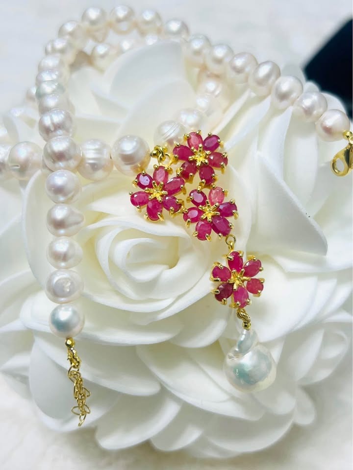 Natural freshwater pearl and ruby necklace with a detailed flower pendant and gold clasp on white.