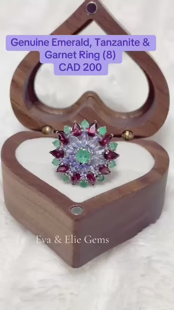This unique ring has a floral cluster of vibrant tanzanite, green emeralds, and pink rhodolite garnets.