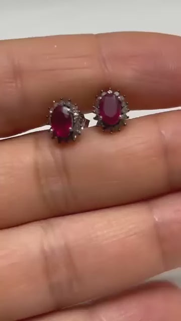 Classic small stud earrings with a central ruby gemstone surrounded by a halo of brilliant diamonds.
