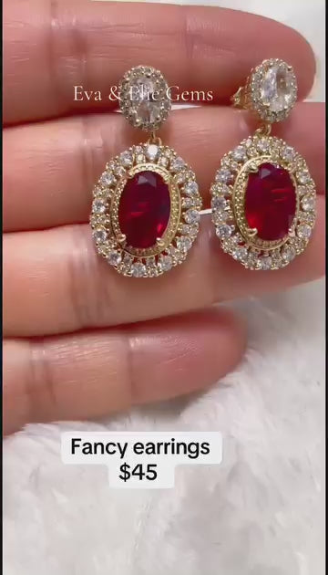 Fancy gold-plated drop earrings with a large red center stone and a sparkling halo.