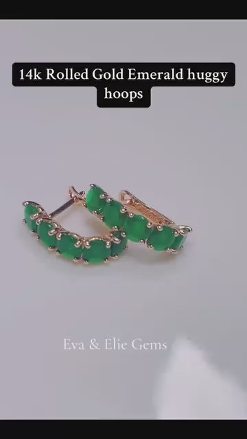  A pair of 14k rolled gold huggie hoops featuring a beautiful line of emerald gemstones