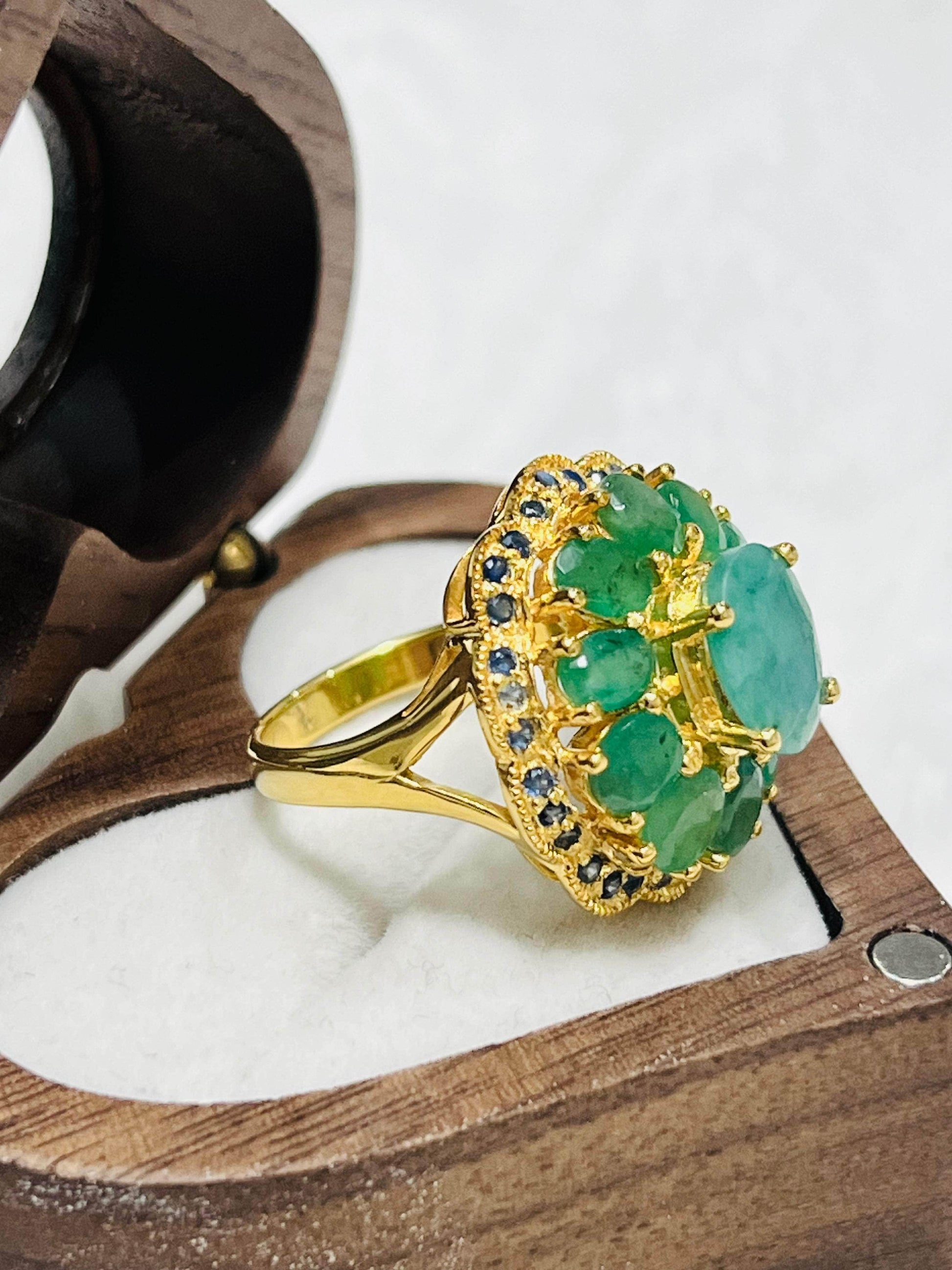 Profile view of a gold ring with emeralds and small gemstones, elegantly set in a classic open wooden jewelry case for display.