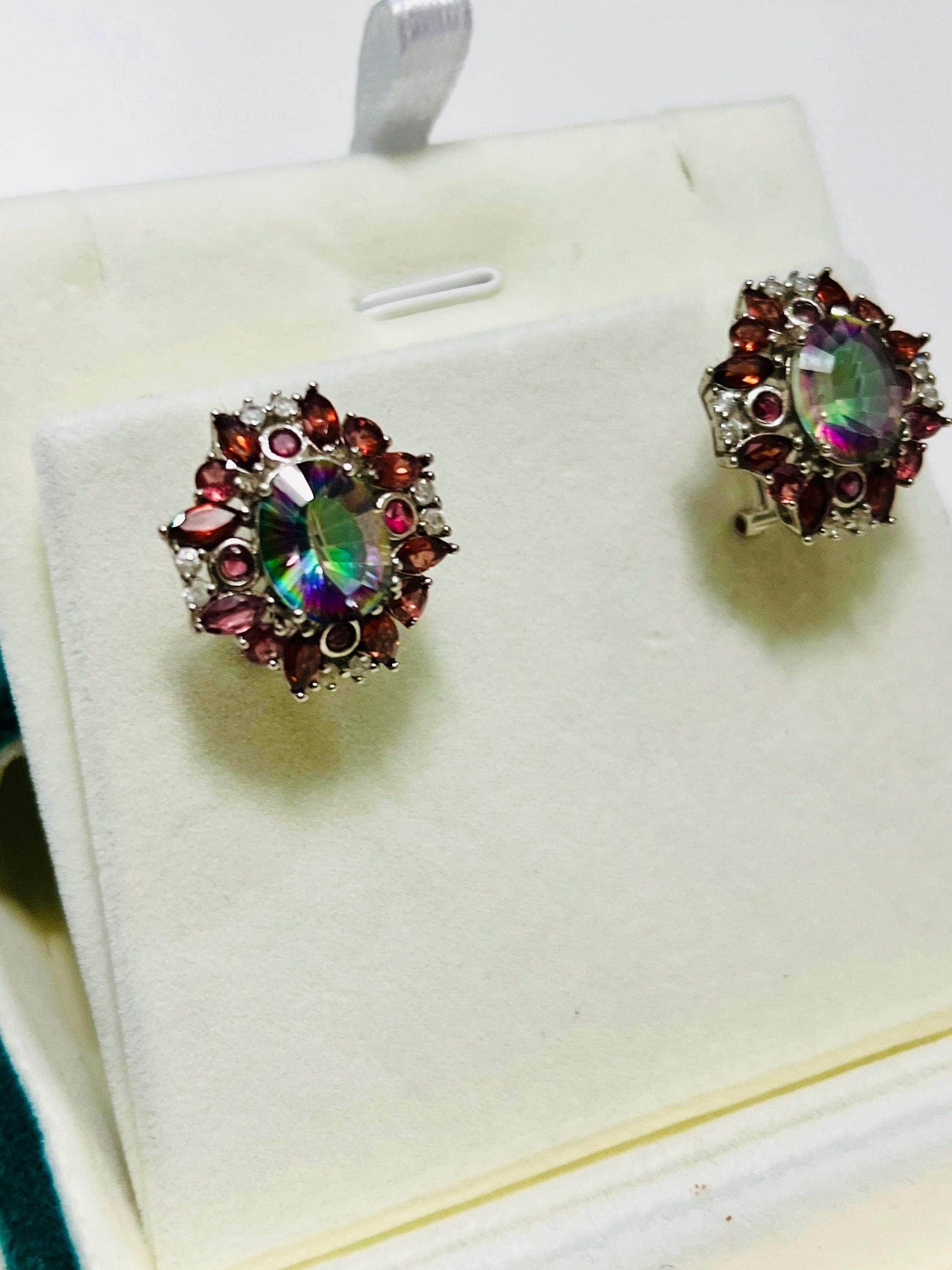 Angled view of rainbow quartz and garnet omega-back earrings, showcasing vibrant colors on a jewelry stand.