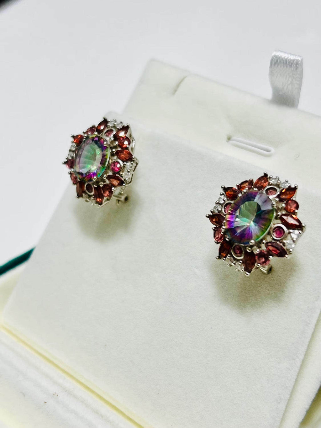 Side view of dazzling rainbow quartz and garnet omega-back earrings on a white display. Elegant gemstone jewelry.