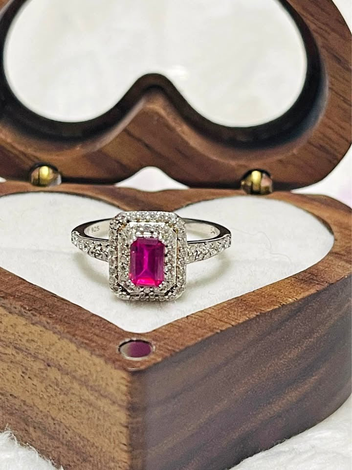 Beautiful natural ruby ring with a diamond-studded halo and band, sitting in a wooden heart box.