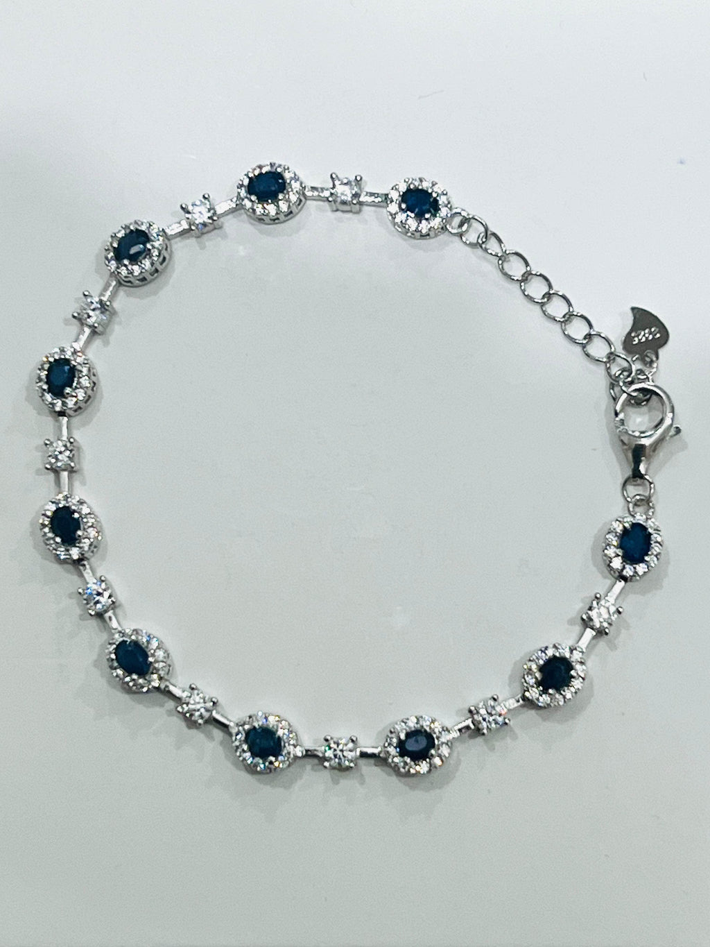  Full-length view of a sparkling rhodium-plated bracelet adorned with round sapphire and clear accent stones.