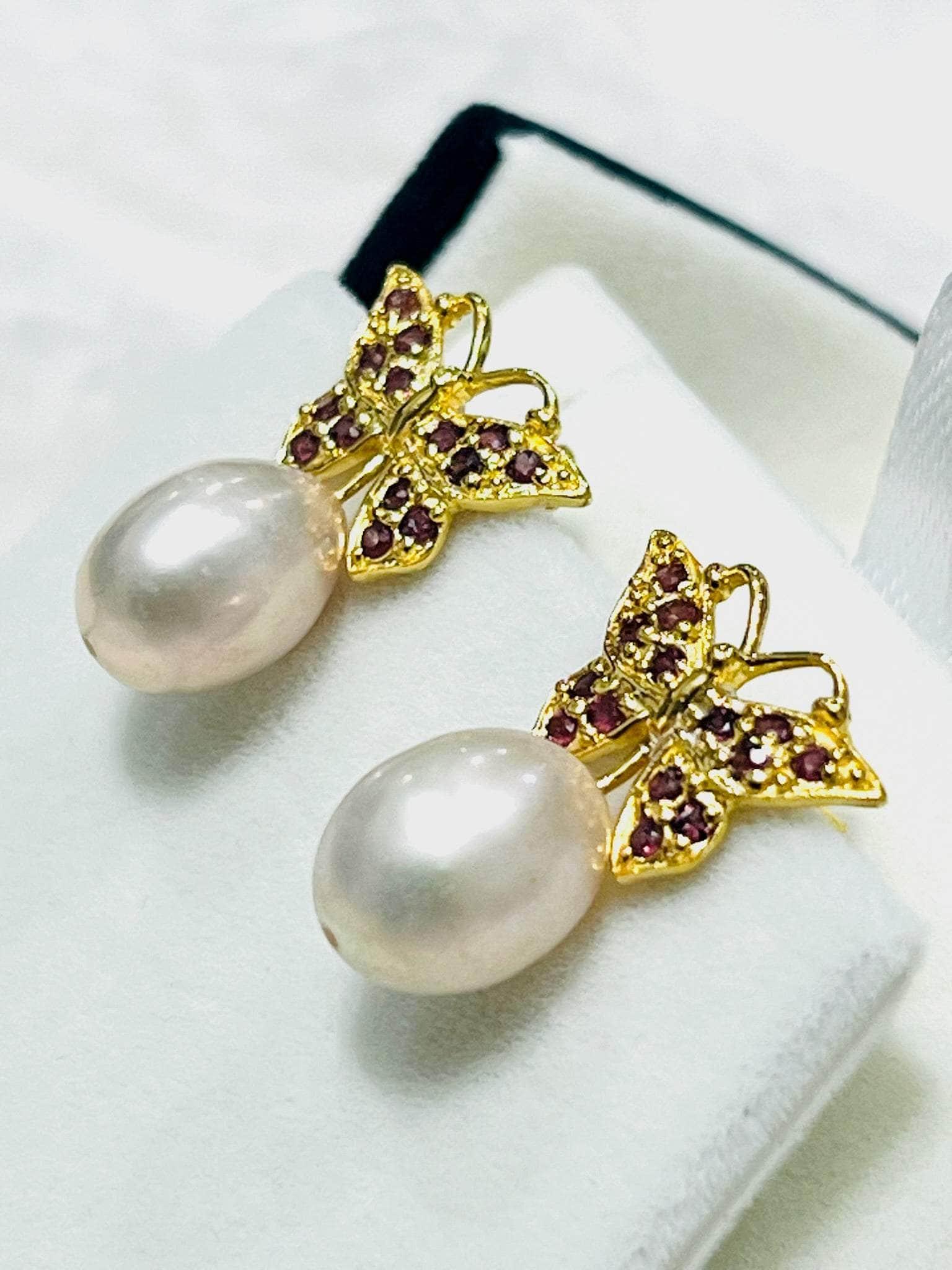 Angled view of rhodolite garnet and gold butterfly earrings, showcasing the unique shape of their natural pink pearl drops.