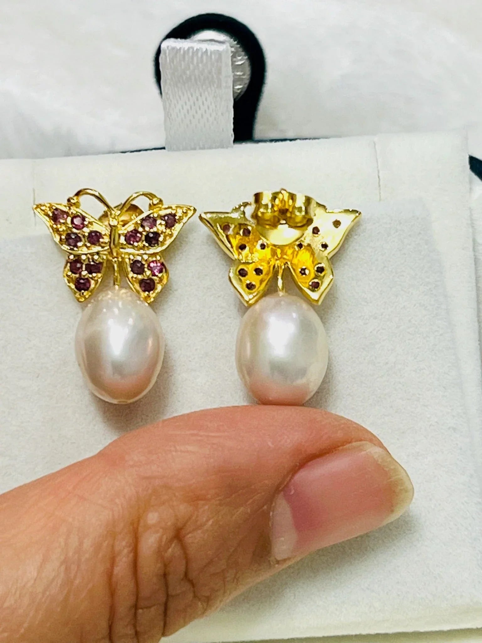 Rhodolite garnet butterfly earrings with pink pearl drops held by hand, revealing the detailed craftsmanship of the back.