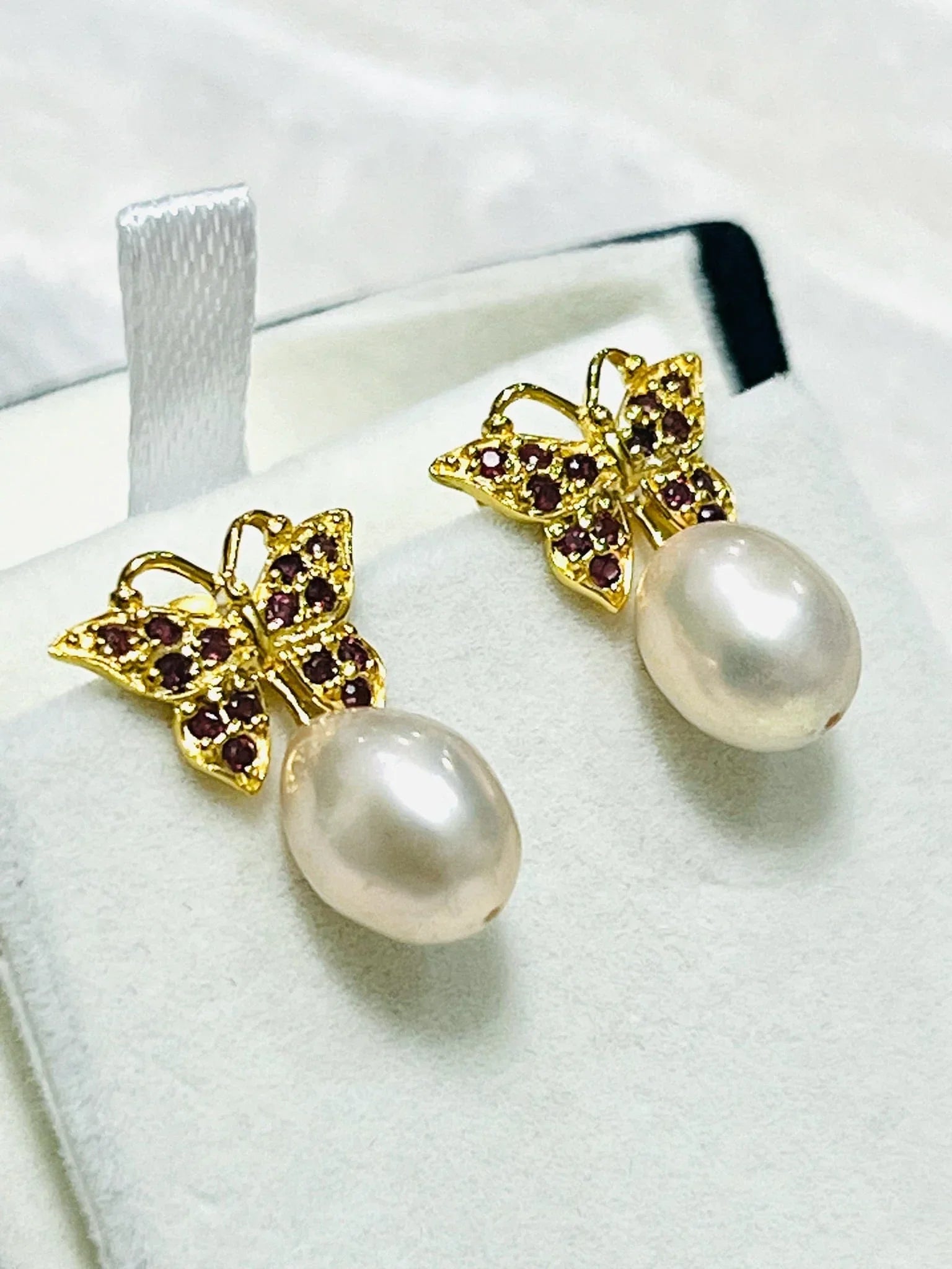 Side profile of gold butterfly earrings adorned with rhodolite garnets and dangling natural pink pearl gemstones.