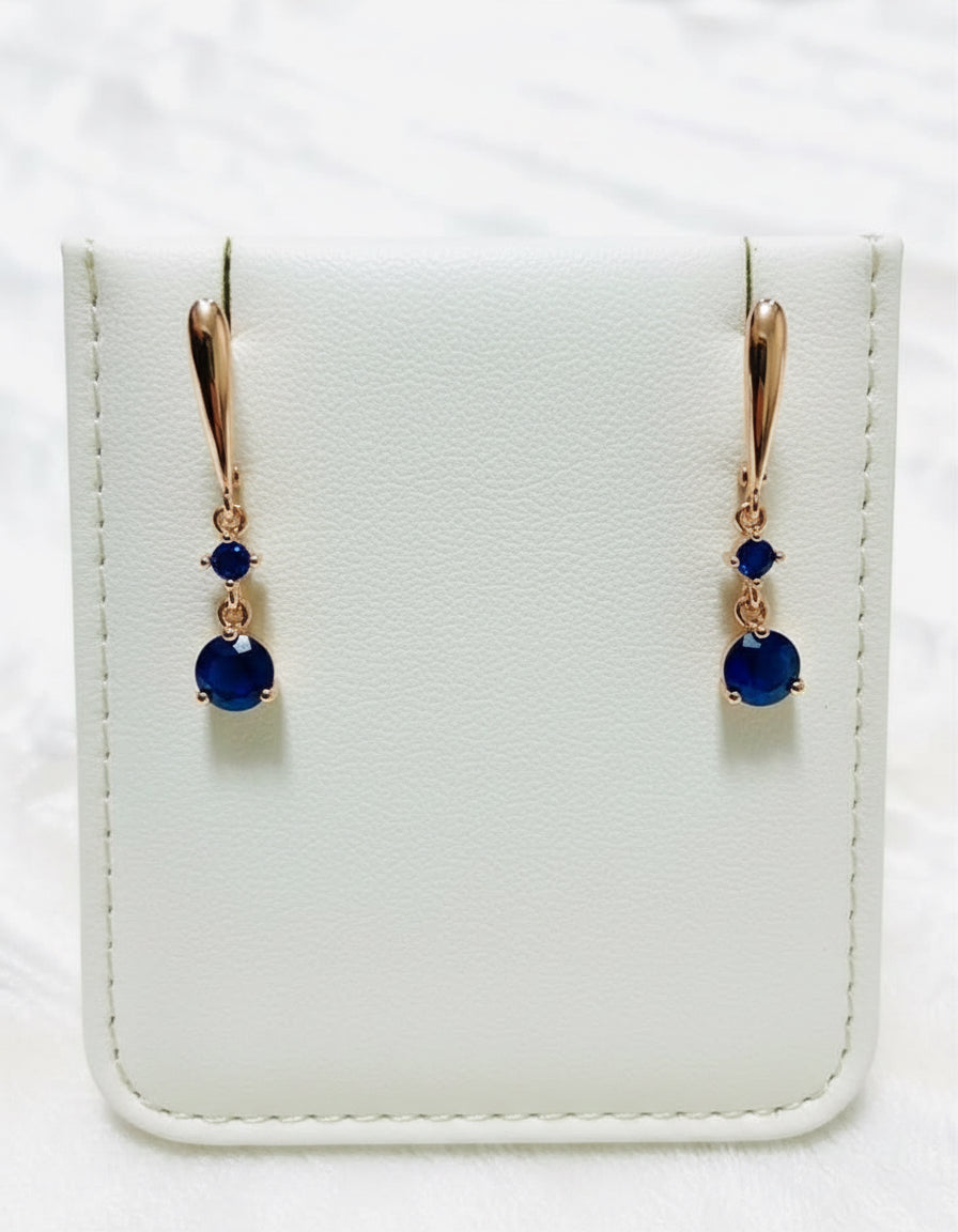 Elegant rose gold drop earrings featuring deep blue sapphire stones, beautifully displayed in a jewelry box.