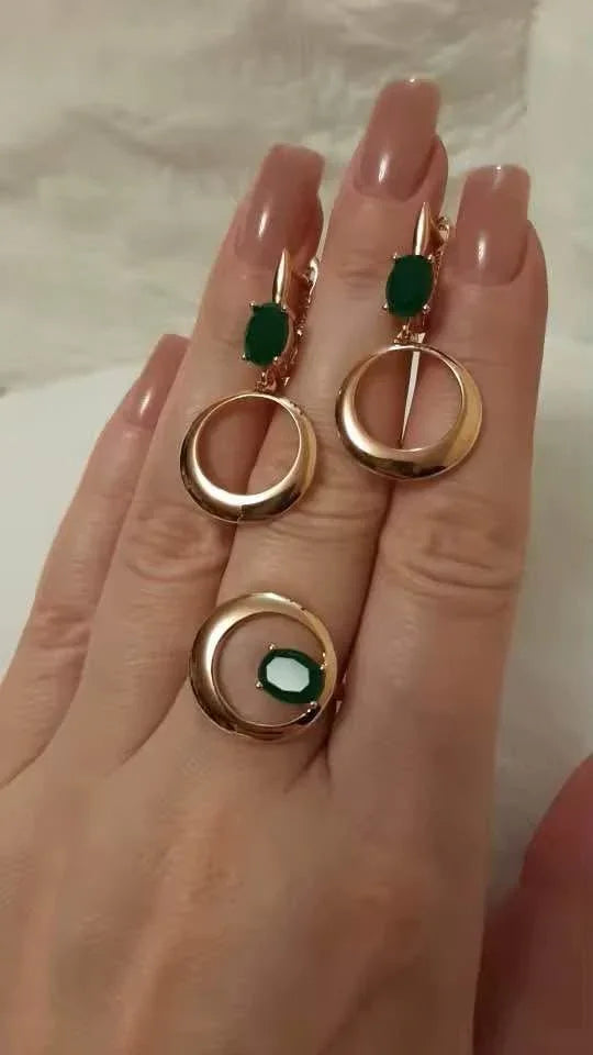 Close-up of a hand wearing the matching rose gold emerald earrings and ring jewelry set.