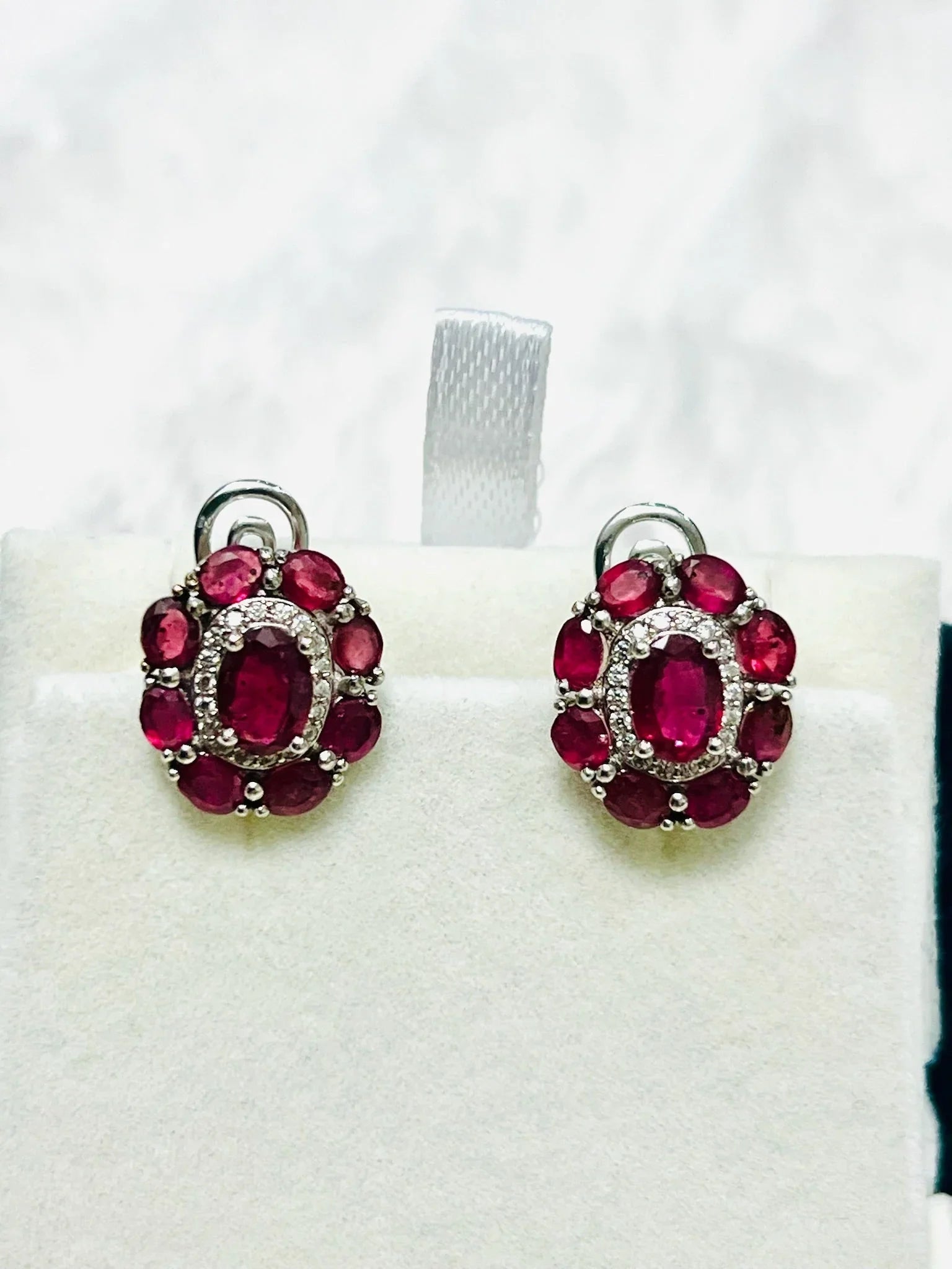 Pair of stunning ruby and diamond halo earrings with oval center rubies, set in sterling silver, displayed from a front view