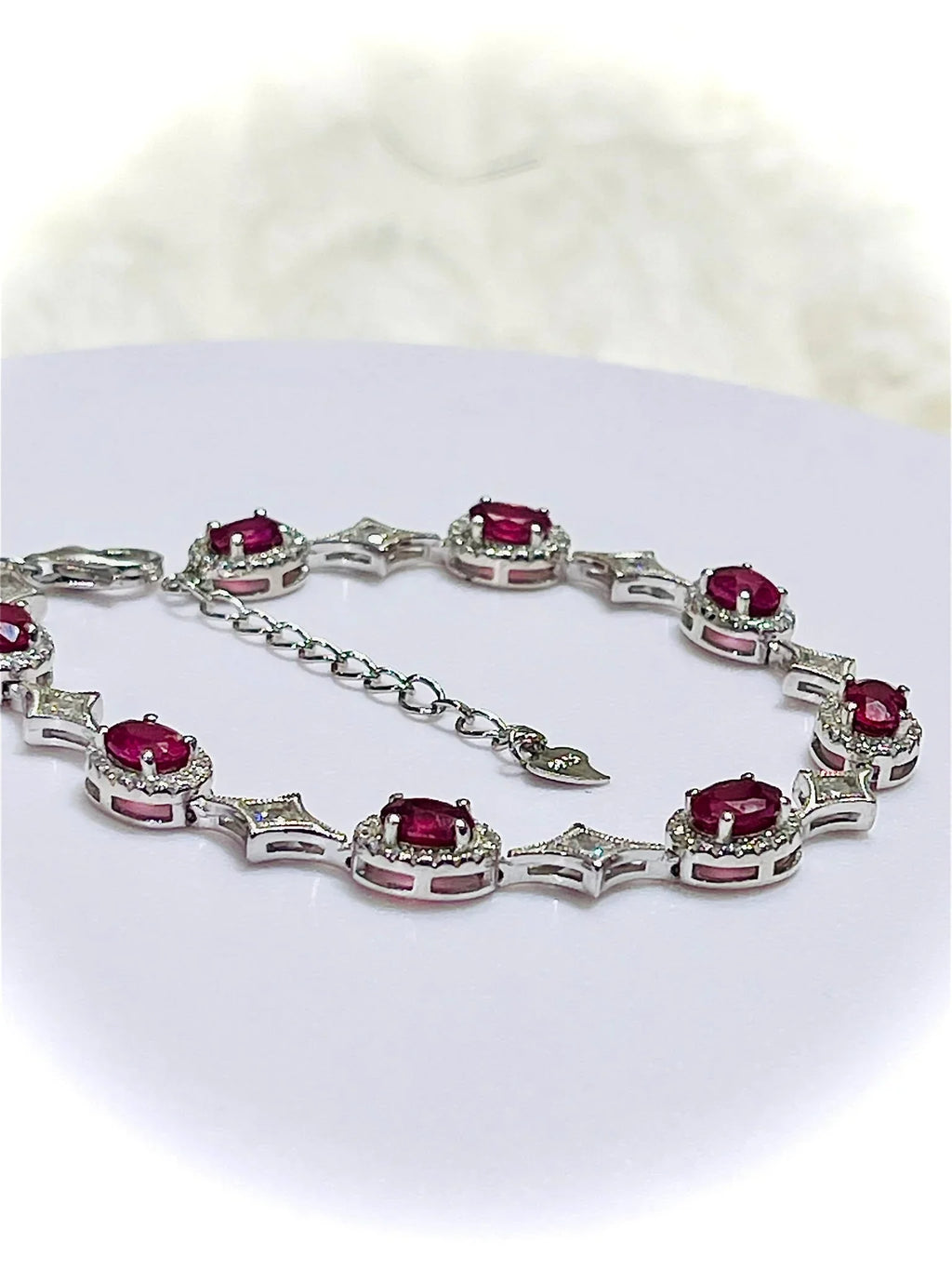 Ruby and diamond silver bracelet displayed on a white surface, showcasing its design, clasp, and adjustable extender chain.