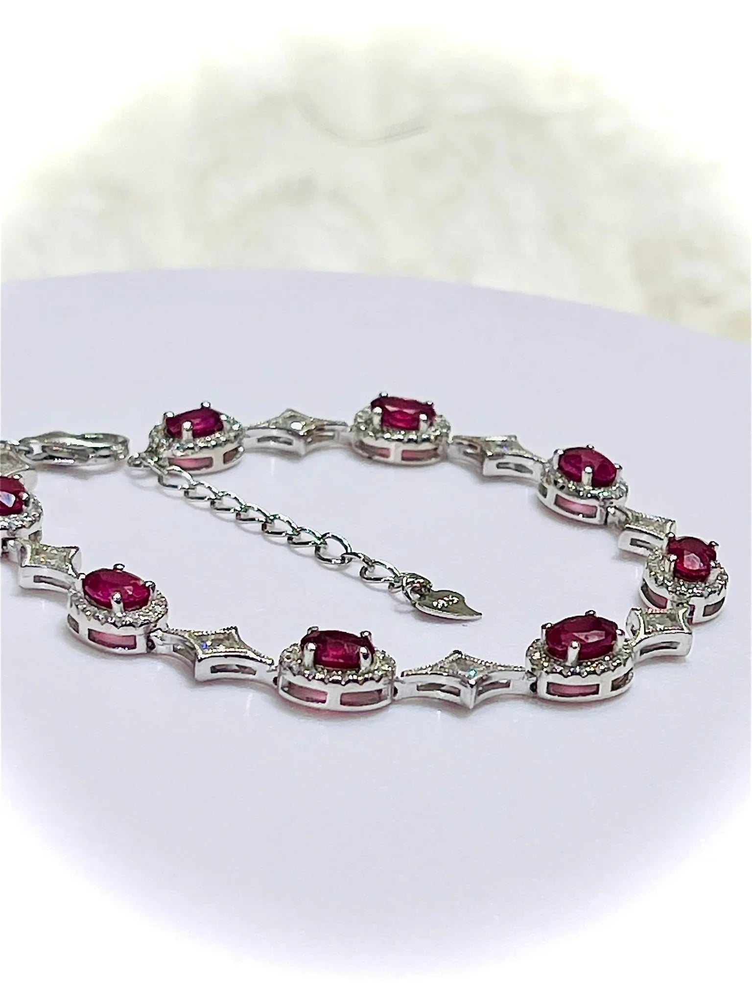 Ruby and diamond silver bracelet displayed on a white surface, showcasing its design, clasp, and adjustable extender chain.