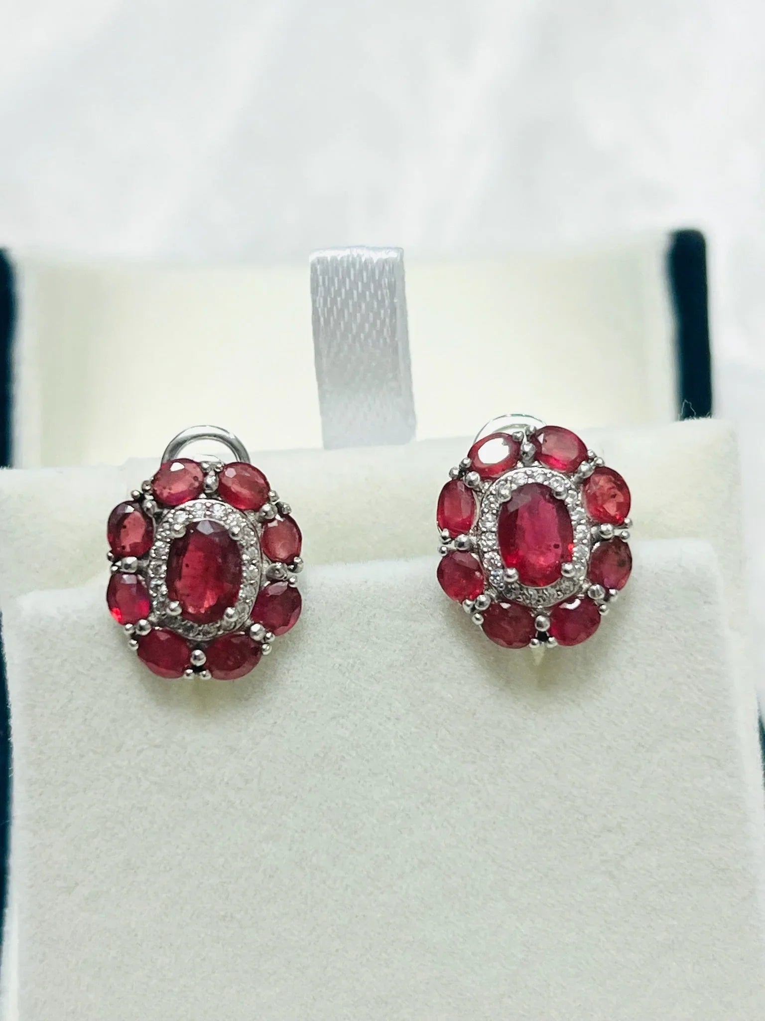 Detailed view of the ruby and diamond halo earrings on a jewelry display, showcasing their vibrant color and elegant design