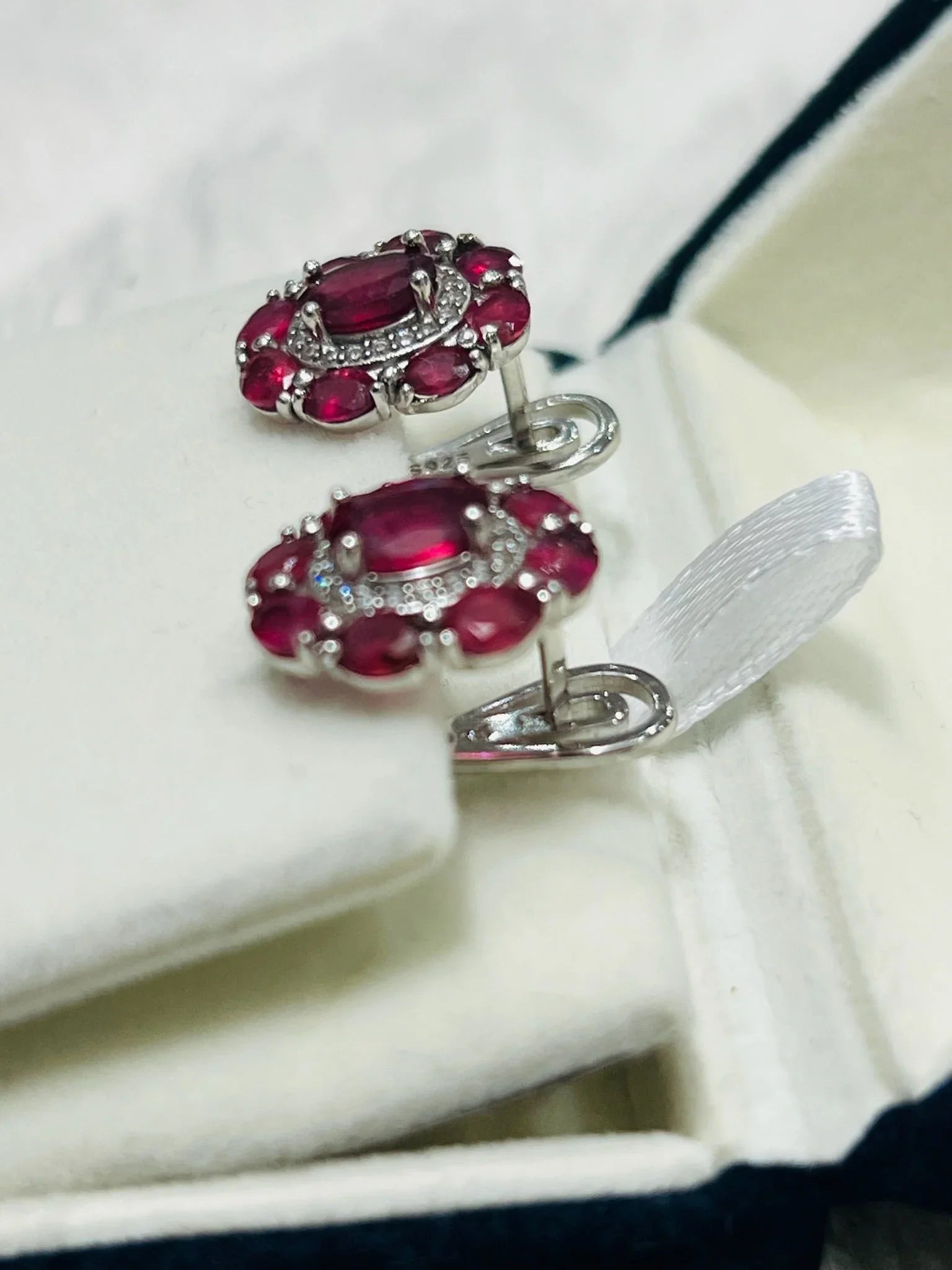Pair of ruby and diamond halo earrings elegantly displayed in a white jewelry box with a ribbon, ready for gifting