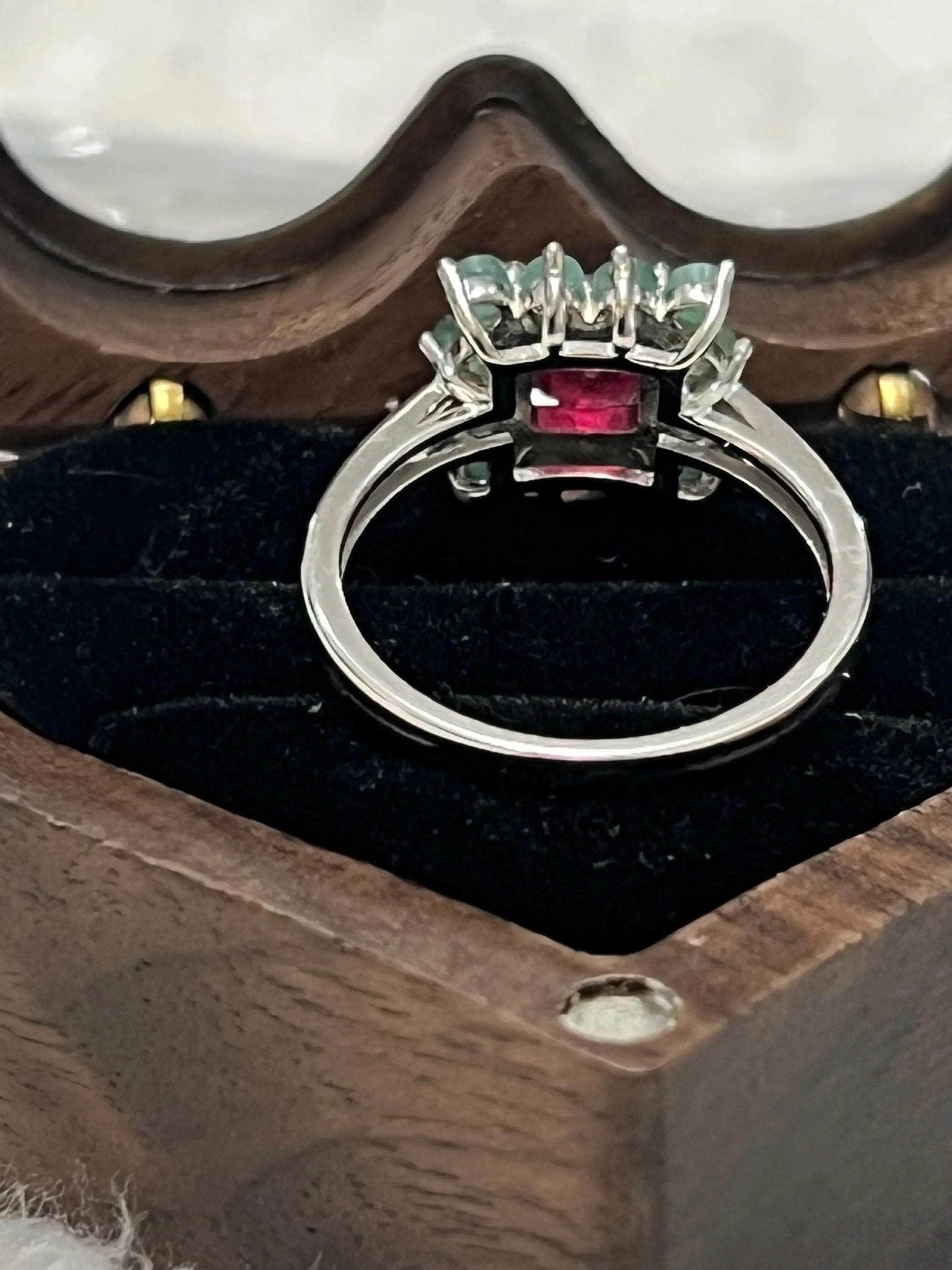 Back view of a handmade ruby and emerald ring, highlighting the craftsmanship and silver band in a box.