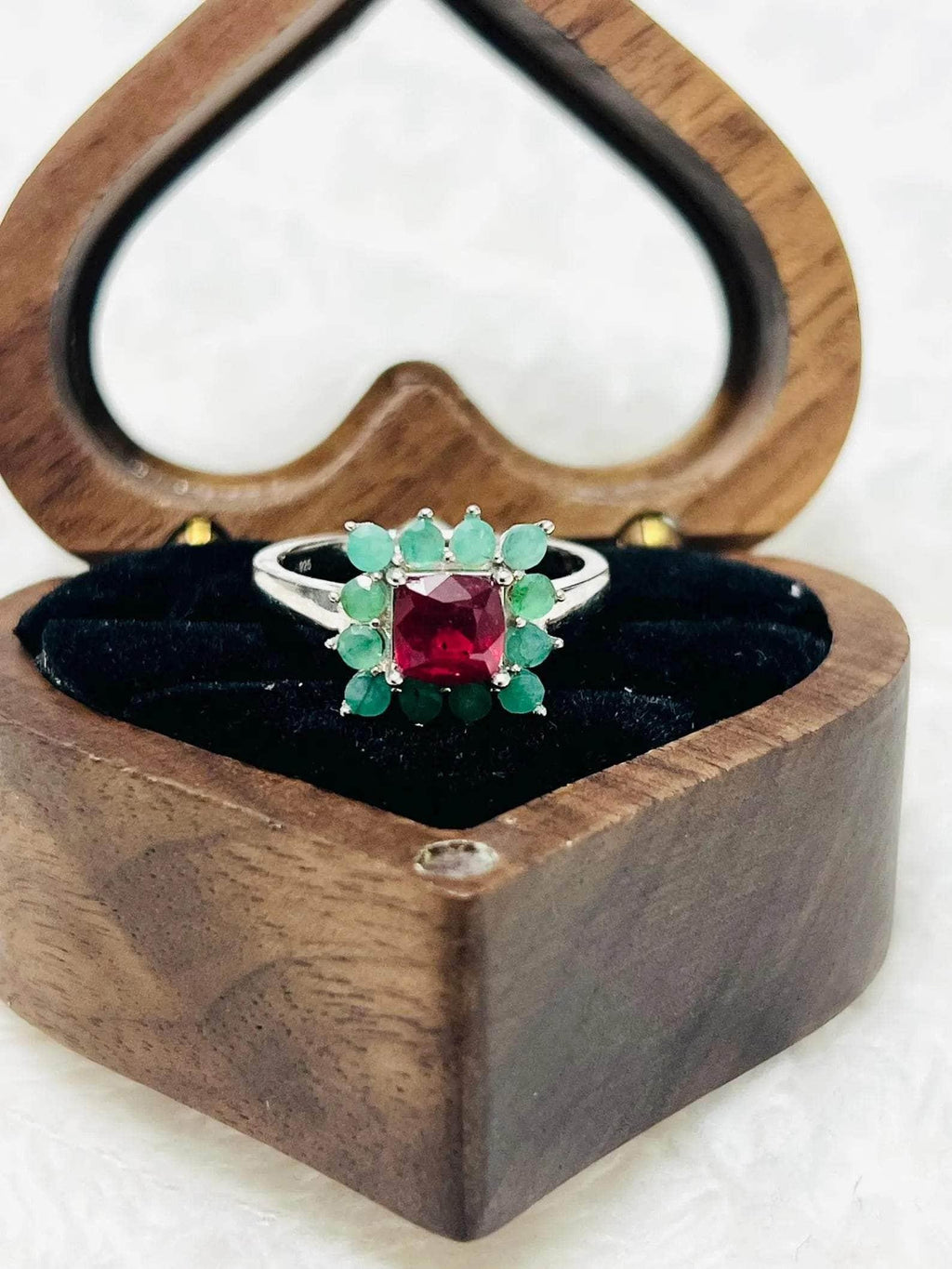 Angled view of a handmade ruby and emerald sterling silver ring inside a unique heart-shaped wooden box.