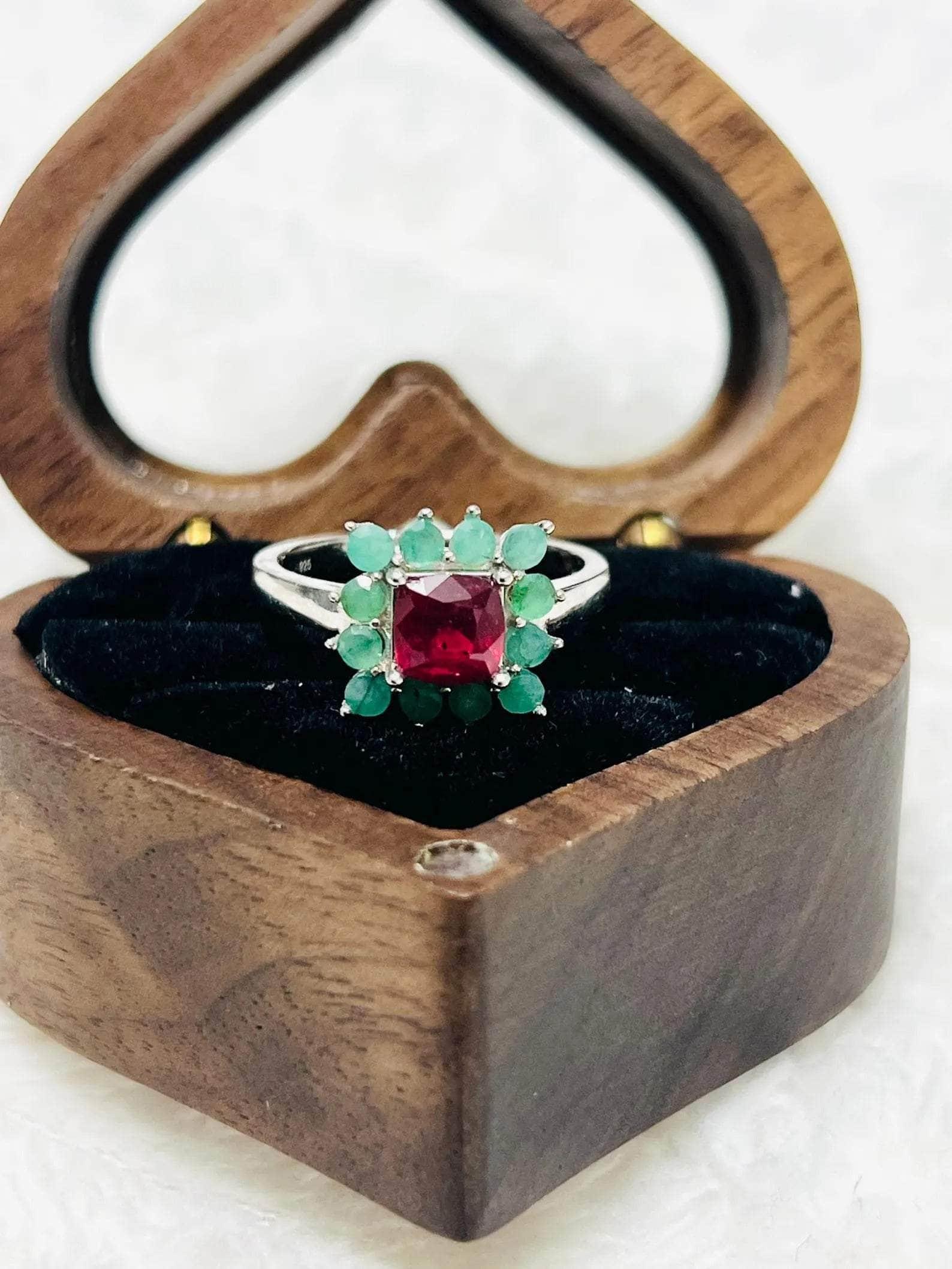 Angled view of a handmade ruby and emerald sterling silver ring inside a unique heart-shaped wooden box.