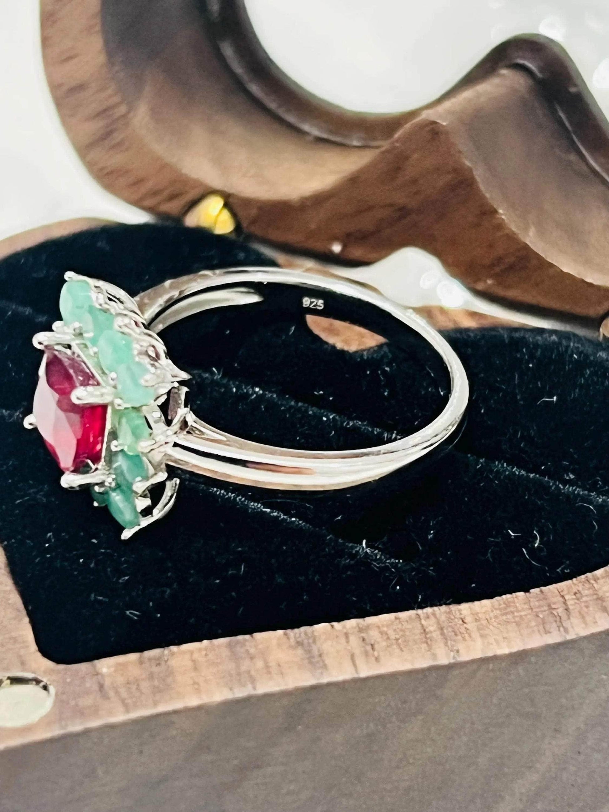 Side view of a handmade ruby and emerald ring, showcasing its silver band and gemstone setting on display.