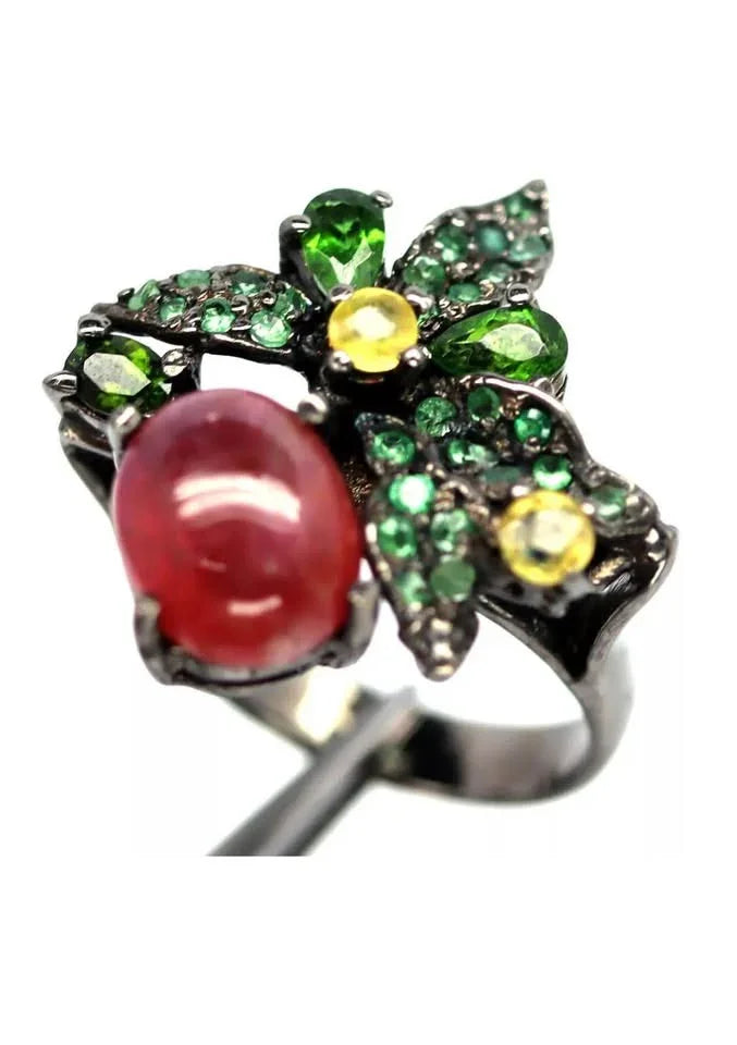  A ring featuring a central ruby with a floral motif of green emeralds and yellow sapphire gems.