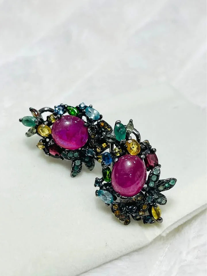 Statement earrings featuring a central ruby cabochon surrounded by an array of colorful emerald and sapphire stones.