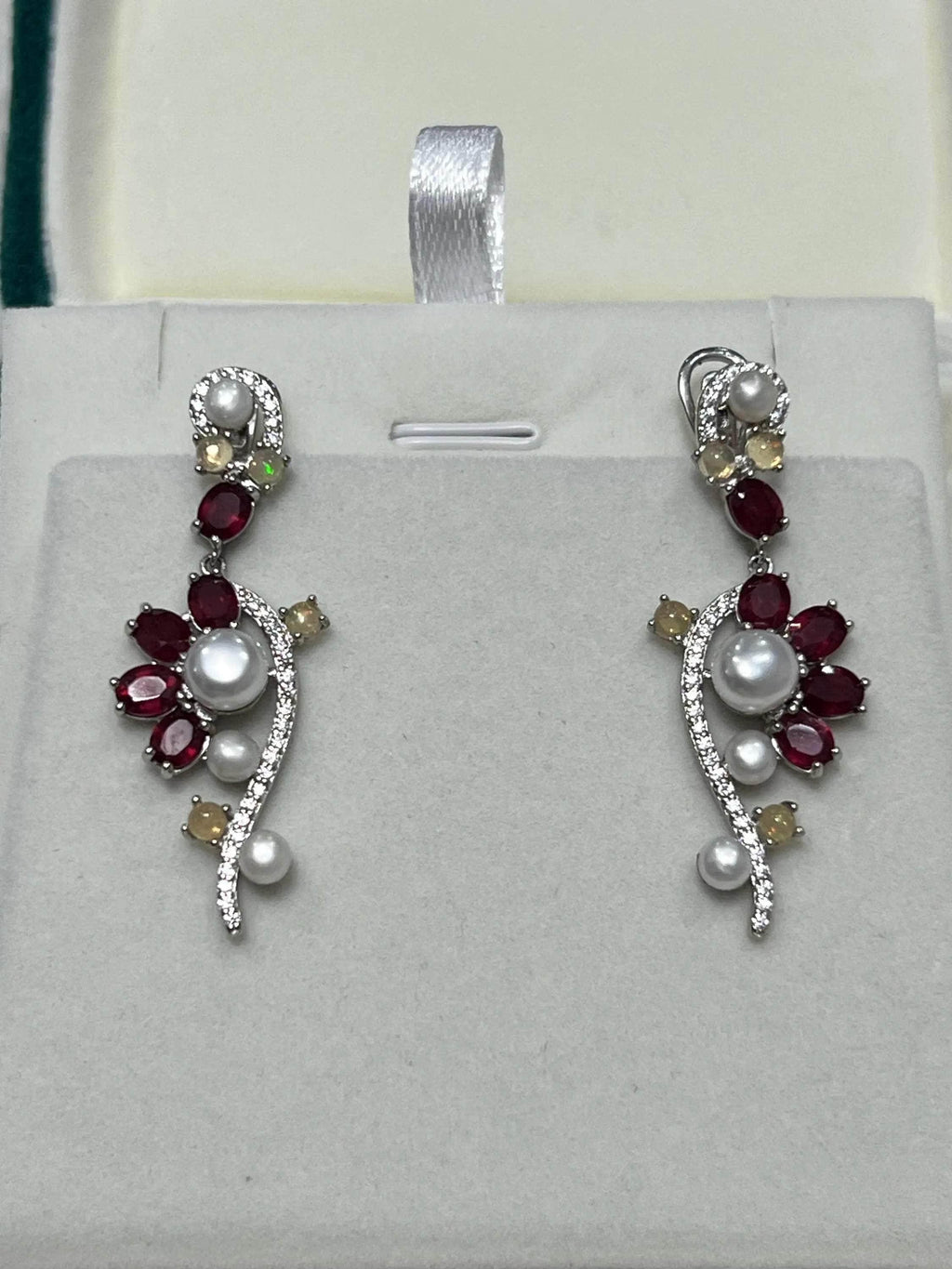 Close-up of exquisite long earrings featuring red rubies, iridescent opals, and lustrous pearls on display.