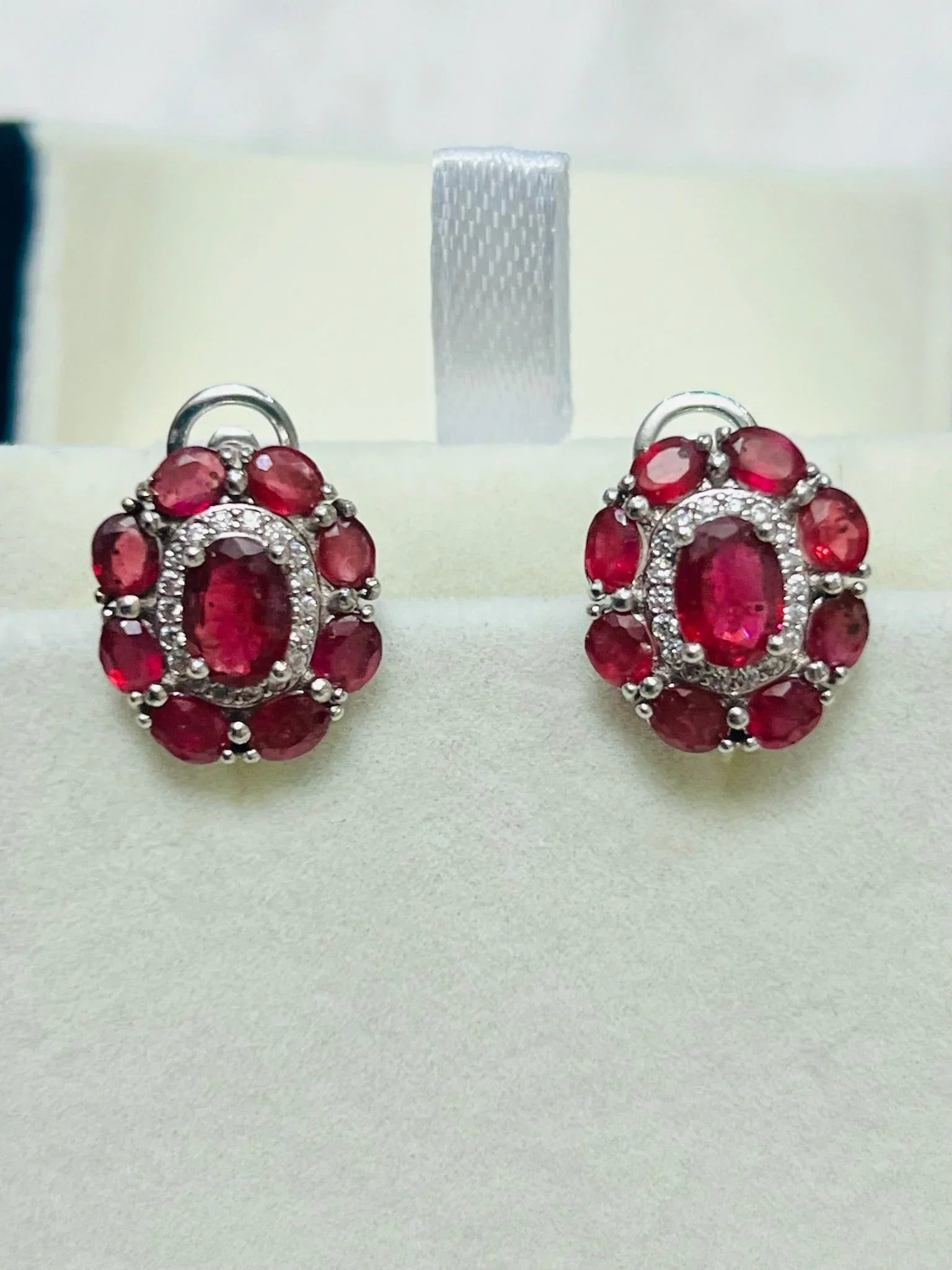 Close-up top view of the ruby and diamond halo earrings, emphasizing the vibrant oval central ruby and surrounding smaller rubies.