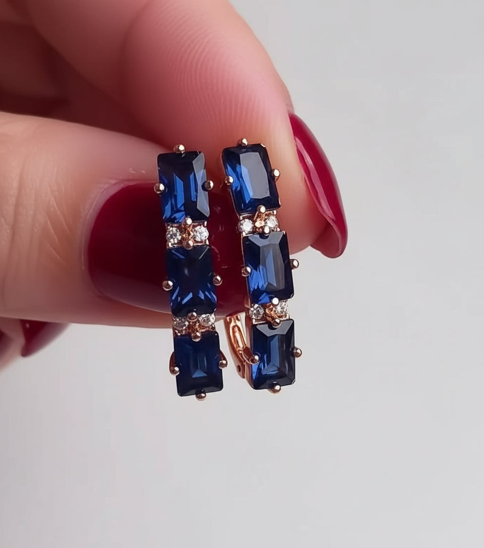 Close-up of 14K rose gold-filled statement earrings adorned with deep blue rectangular sapphires and clear accents.