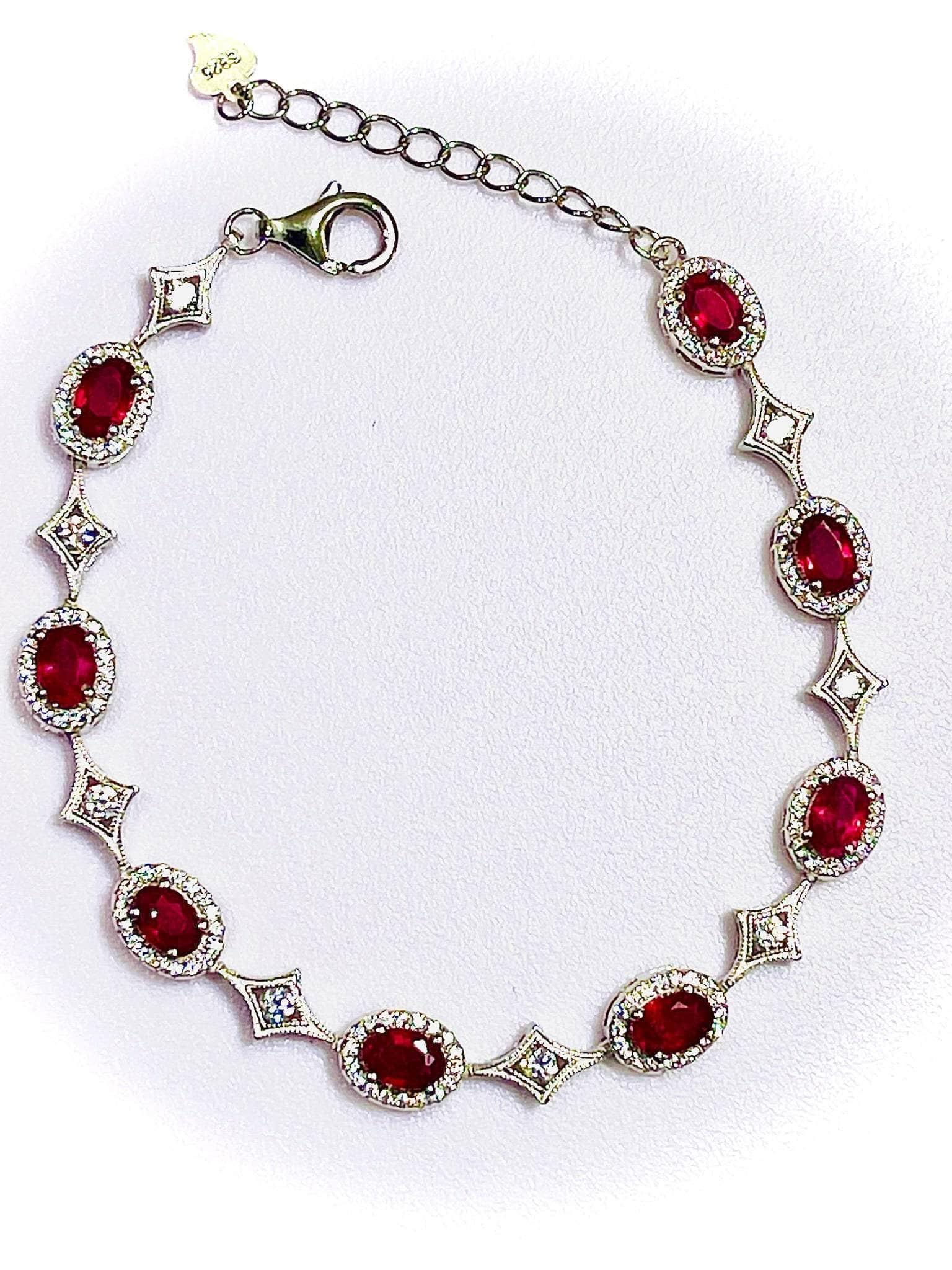 Elegant silver tennis bracelet with oval-cut rubies surrounded by diamonds, featuring a secure clasp and extender chain.