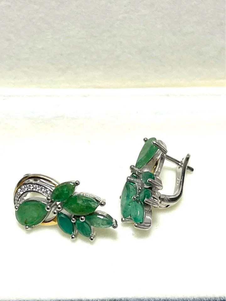 A side view of natural emerald earrings in sterling silver with two-toned gold and silver settings.